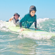 De surfinstructeur kiest de juiste golf uit en geeft het surfboard een duwtje
